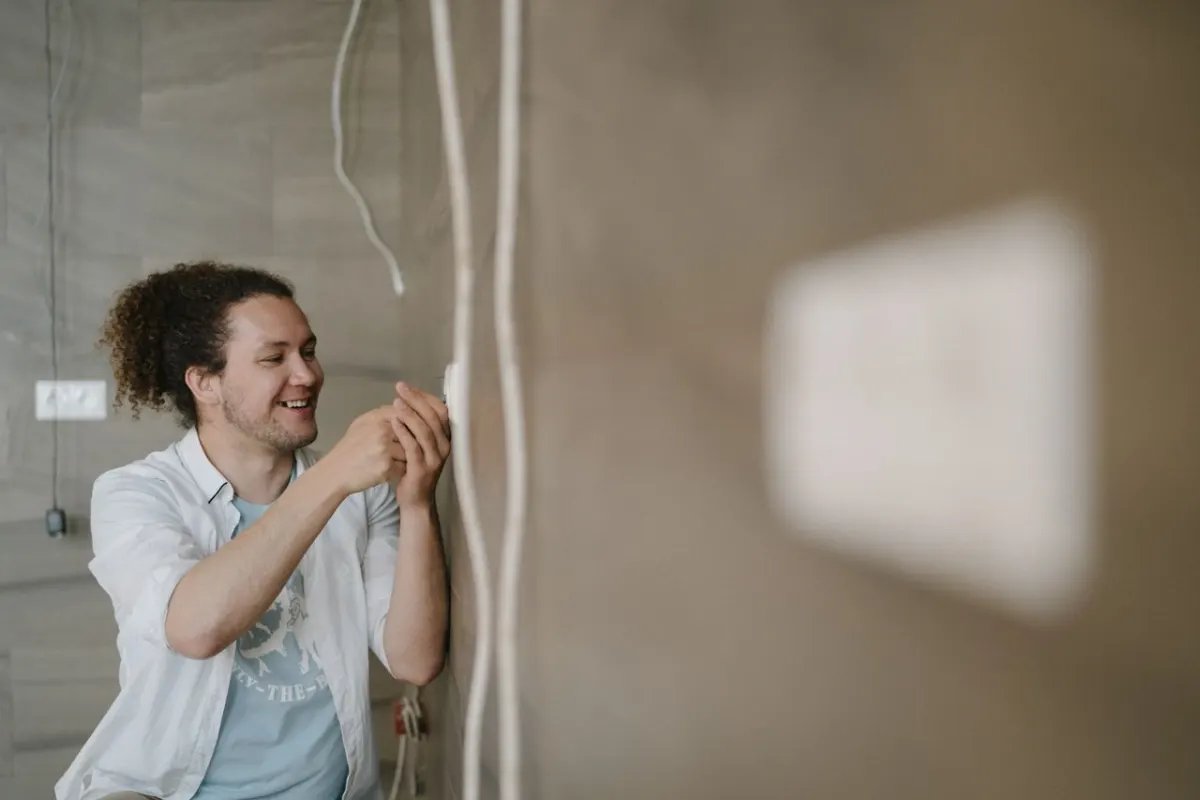 Électricien souriant qui intervient sur une prise électrique au domicile d'un particulier