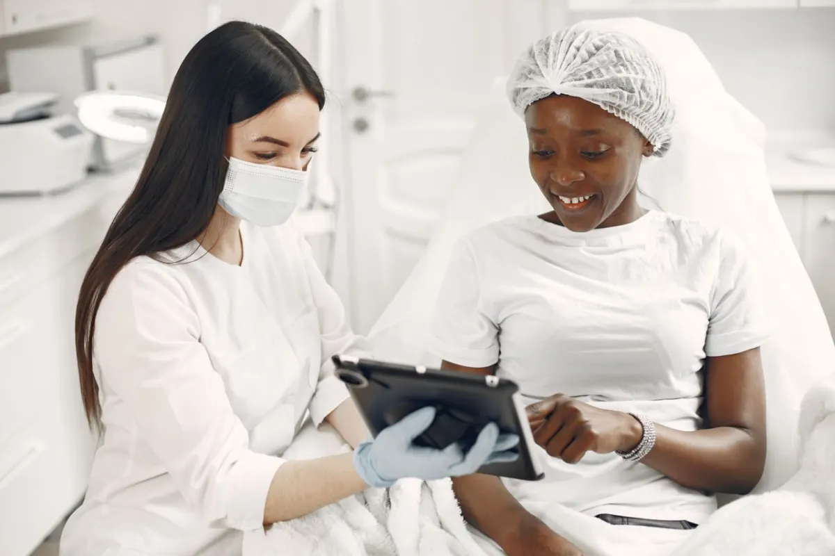Patiente souriante en consultation avec sa dermatologue qui lui présente un soin sur tablette